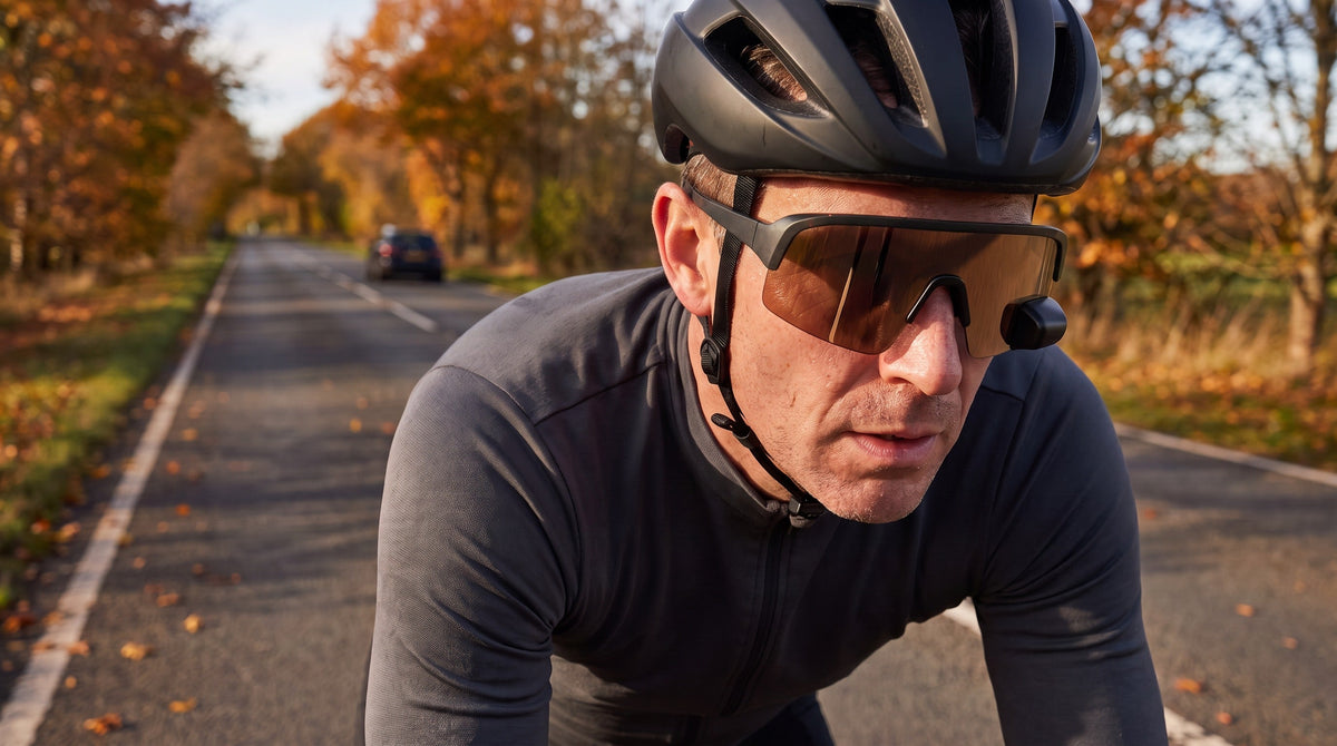A road cyclist on a quiet autumn country road wearing The View sunglasses with a rear-view mirror in the lens, a car far behind