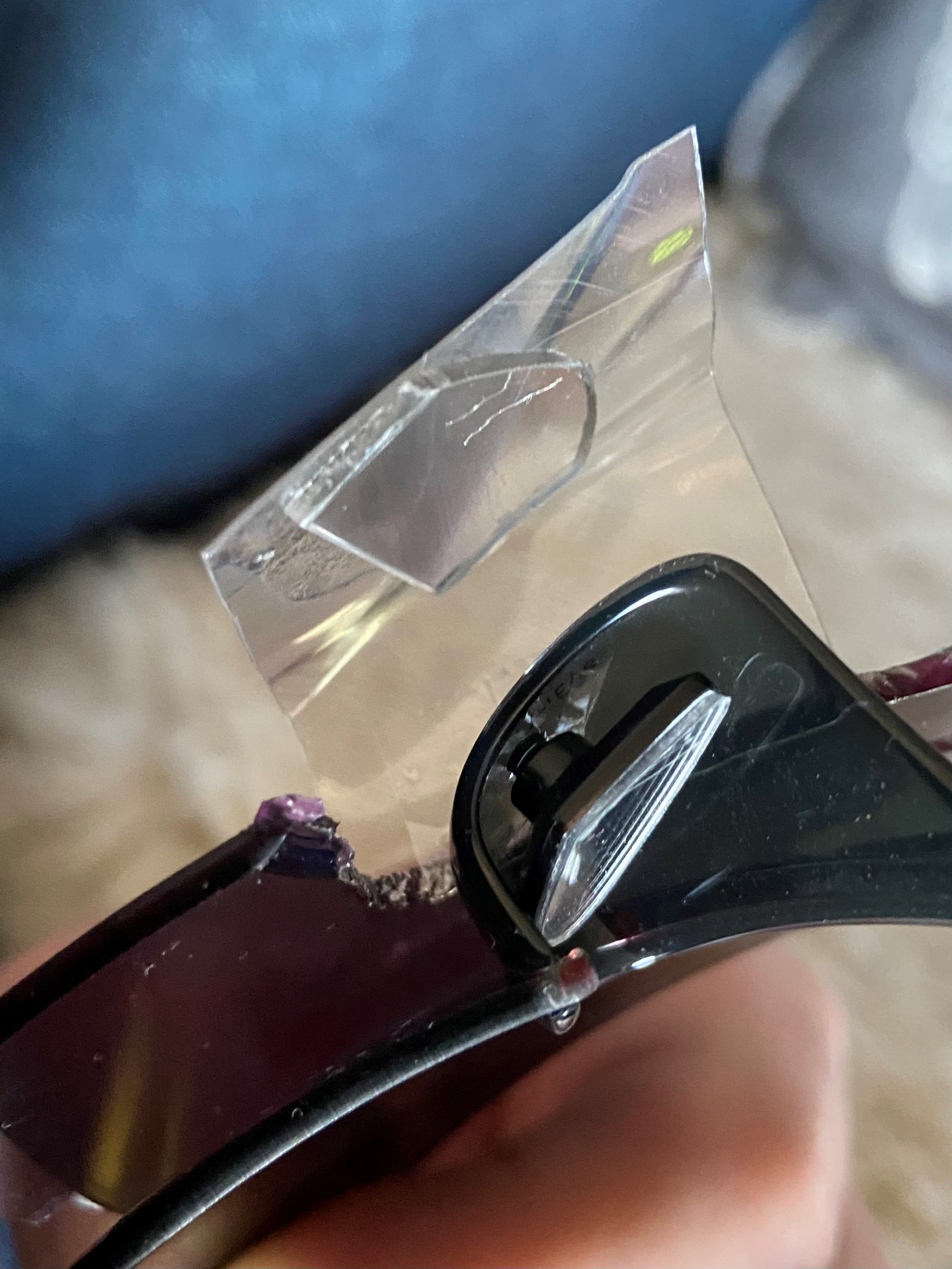 Gros plan sur une paire de lunettes de soleil dont la charnière est cassée, réparée temporairement à l'aide d'un morceau de ruban adhésif transparent pour maintenir la monture ensemble.
